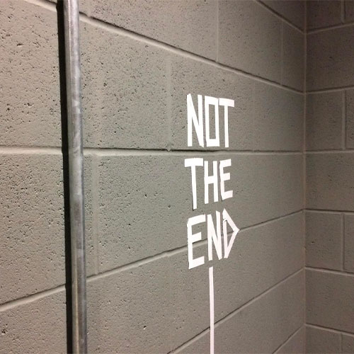 It;s not The end taped in white on a grey brick wall